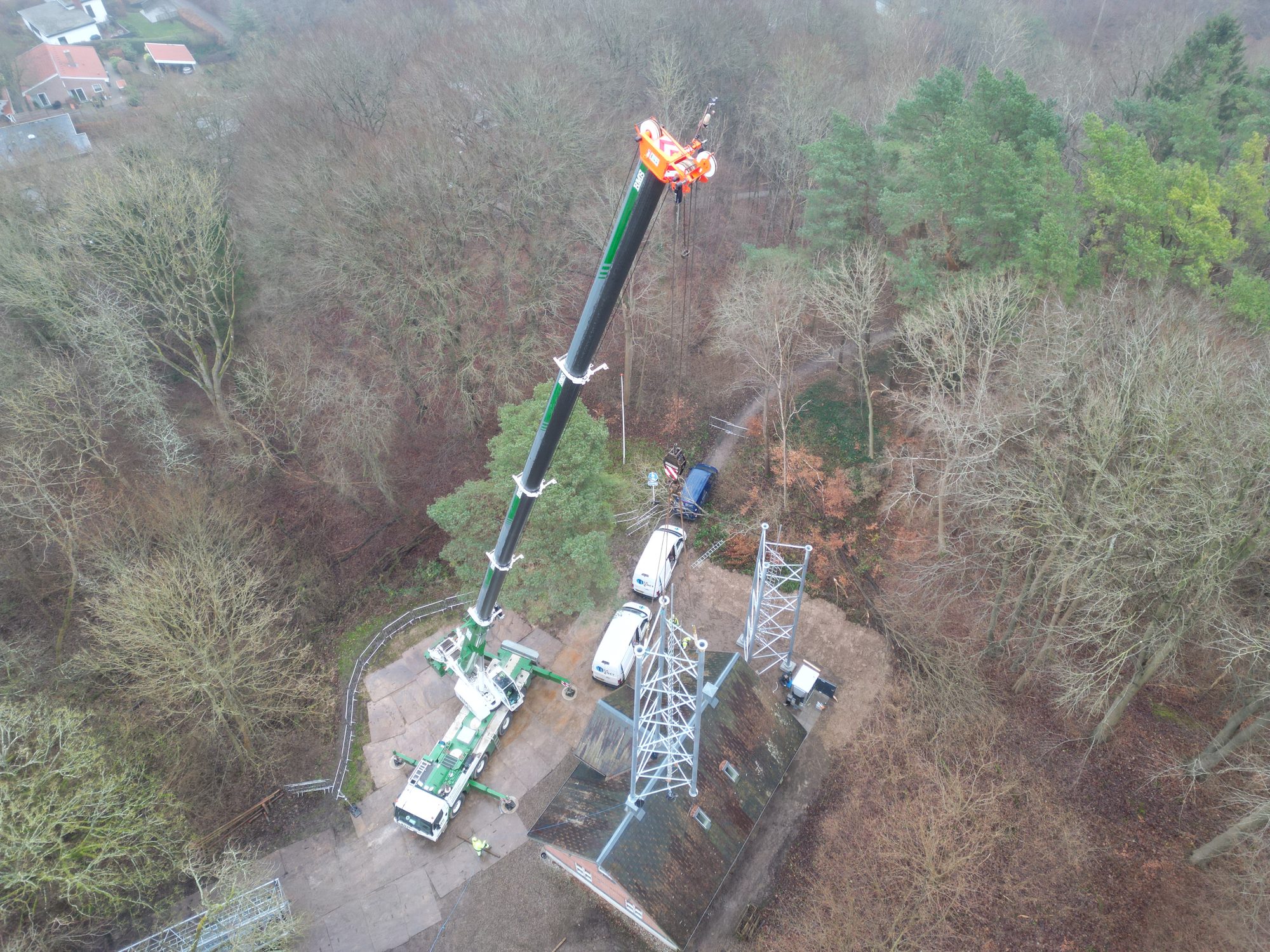 BMS-mobilkran med langt udlæg arbejder ved en telemast omgivet af skov, set fra luften