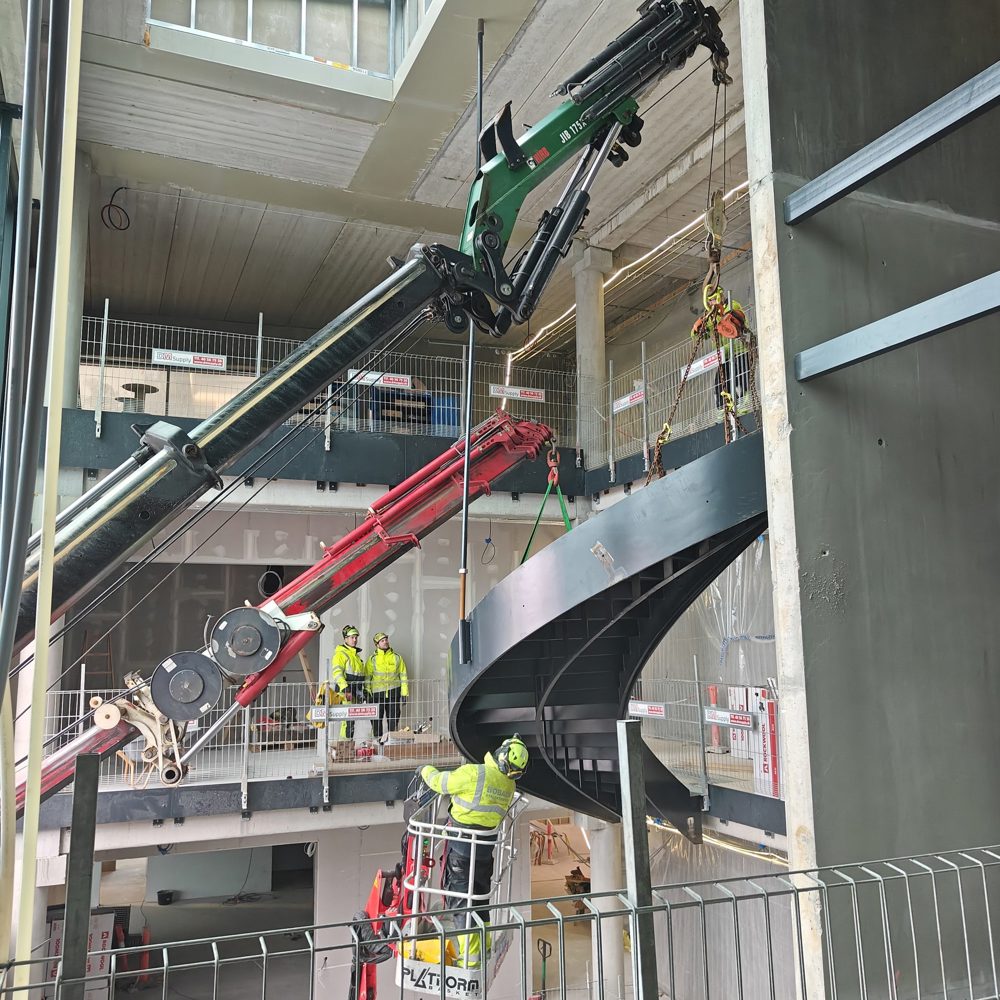 kraner sænker en buet sort stål-trappe på plads i et atrium 