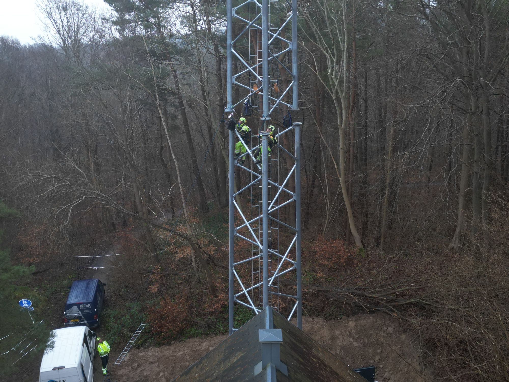 Teknikere arbejder højt oppe på telemast omgivet af skov