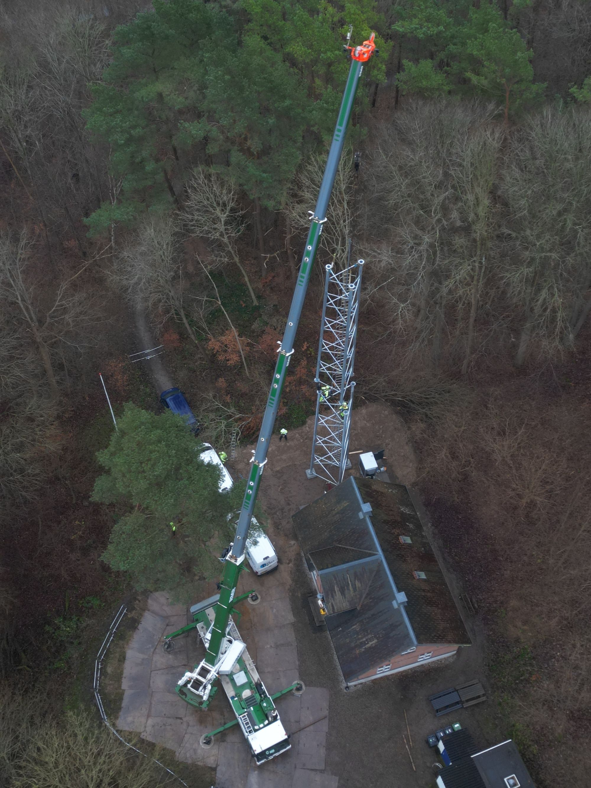Mobilkran monterer telemast tæt på skovbevokset grund set fra luften