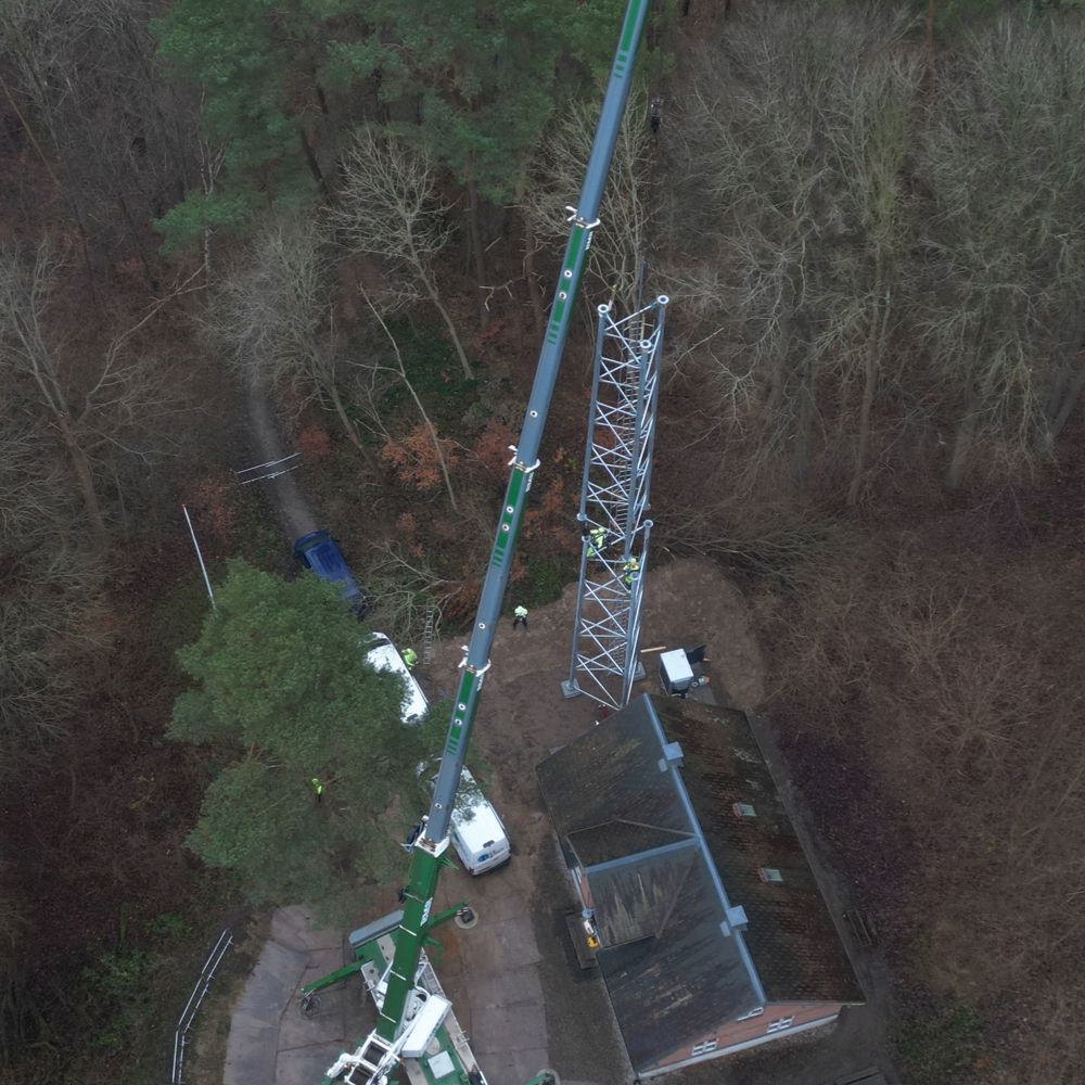 Mobilkran monterer telemast tæt på skovbevokset grund set fra luften