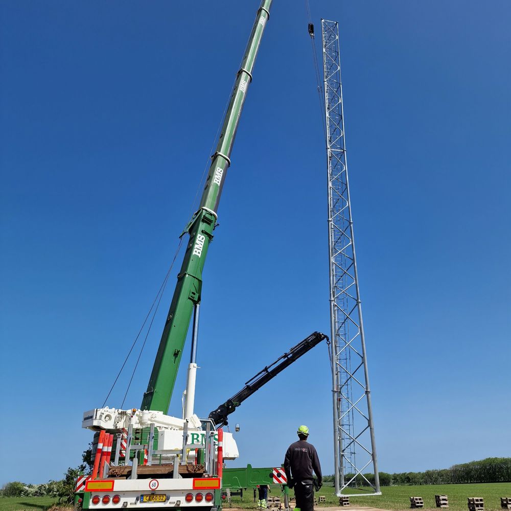 Fuldrejst telemast i markareal, mobilkran og to medarbejdere ved siden af
