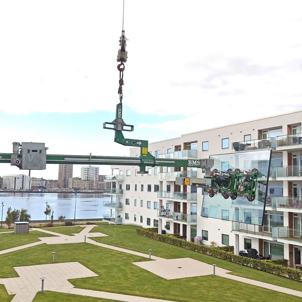 Balanceåg løfter stort glaselement hen til altan på lejlighedsbygning