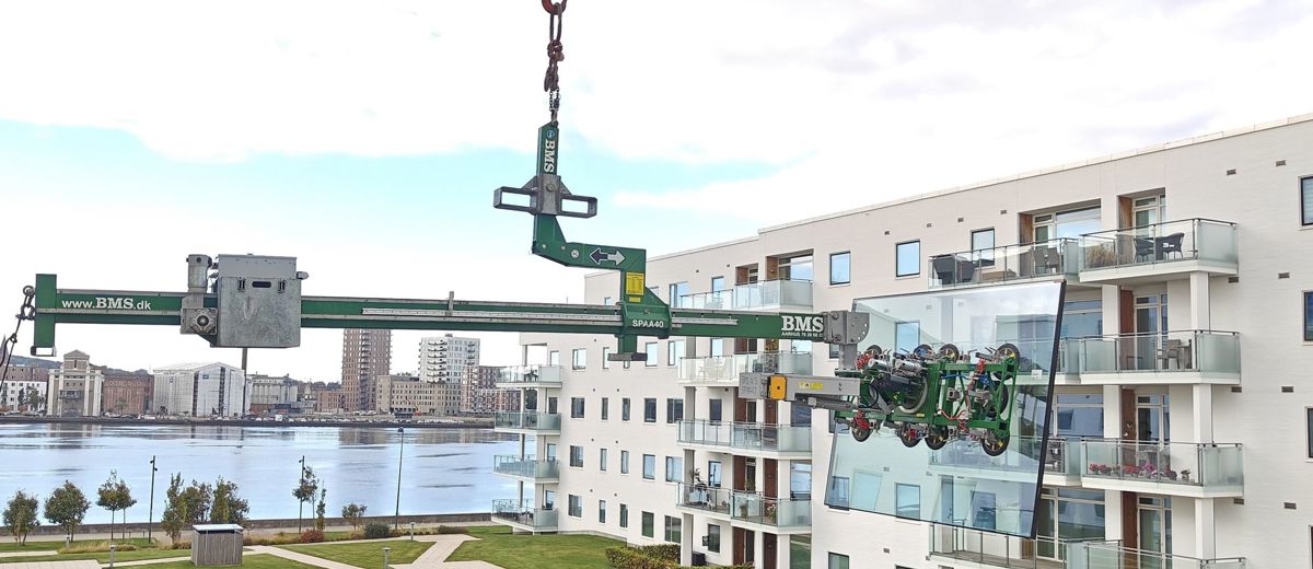 Balanceåg løfter stort glaselement hen til altan på lejlighedsbygning