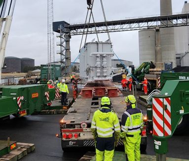 To BMS Krangården-kraner tandemløfter en stor hvid transformer ved kraftværk