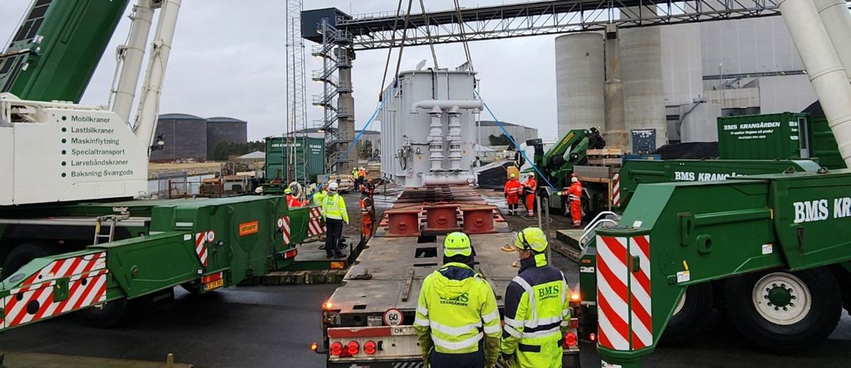 To BMS Krangården-kraner tandemløfter en stor hvid transformer ved kraftværk