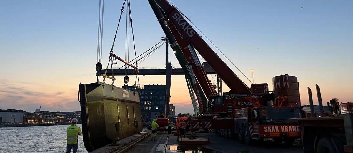 Flere mobilkraner tandemløfter den historiske dokport ved solnedgang i København