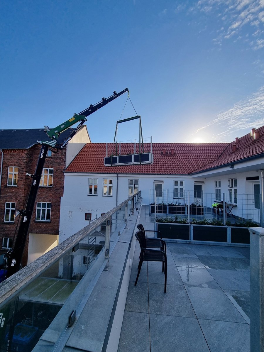 Bæltekran løfter plantekasse fra baggård op på terrasse